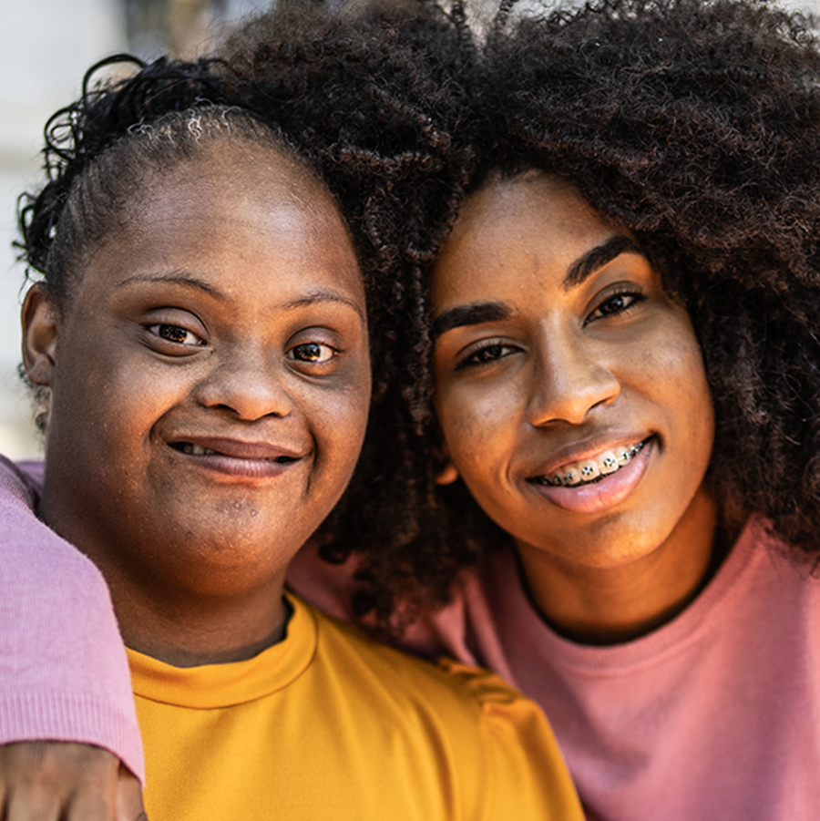 Two African American sisters hugging and smiling. One has Downs Syndrome.